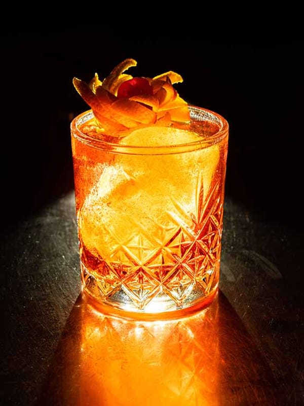 A glowing amber cocktail over ice in a cut-glass tumbler